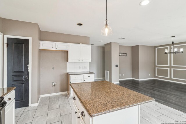 24915 Flying Arrow, San Antonio, TX 78258 - kitchen featuring light stone counters, a center island, baseboards, hanging light fixtures, and white cabinetry