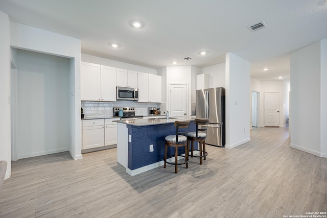 209 Wolf Crst, Seguin, TX 78155 - kitchen with stainless steel appliances, a breakfast bar, light wood finished floors, backsplash, and white cabinetry