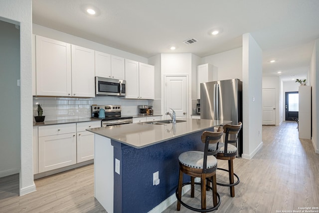 209 Wolf Crst, Seguin, TX 78155 - kitchen featuring stainless steel appliances, tasteful backsplash, a kitchen bar, light wood-style floors, and a kitchen island with sink