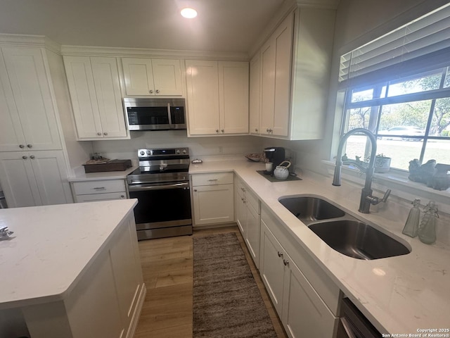 kitchen with wood finished floors, a sink, white cabinetry, and appliances with stainless steel finishes