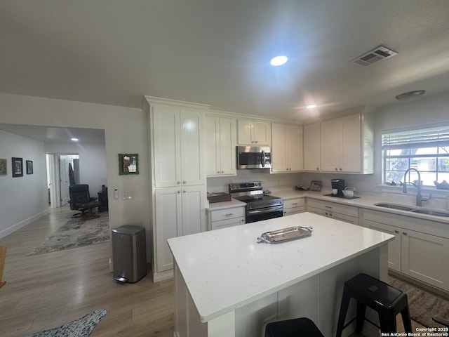 kitchen featuring visible vents, a sink, a center island, appliances with stainless steel finishes, and white cabinetry