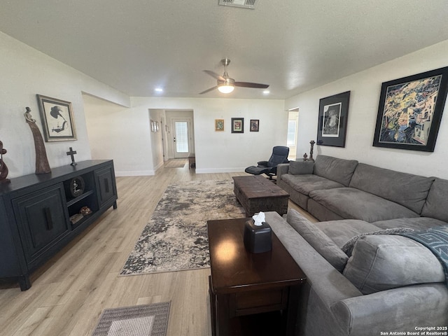 living area featuring light wood-style flooring, visible vents, baseboards, and ceiling fan