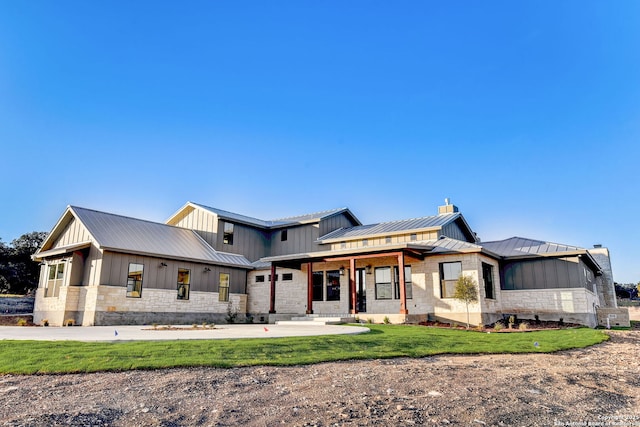 view of front facade with a chimney, a front lawn, stone siding, metal roof, and a standing seam roof