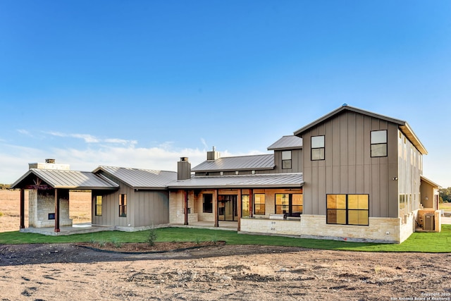 back of property with a standing seam roof, stone siding, a chimney, metal roof, and board and batten siding
