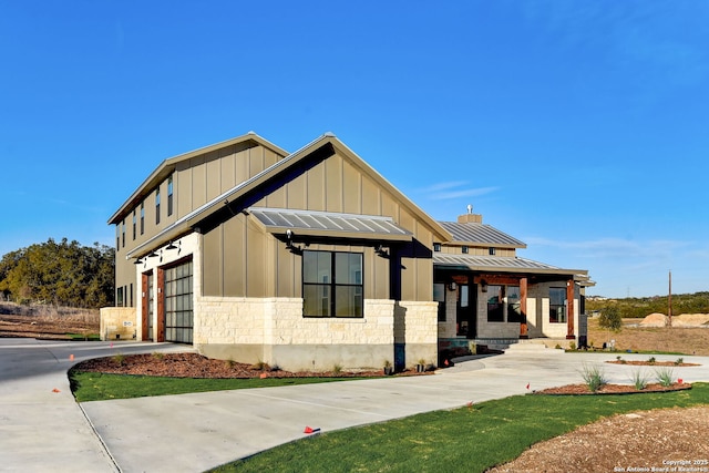 modern farmhouse featuring board and batten siding, driveway, stone siding, and a garage