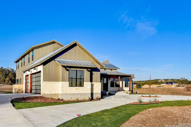 modern farmhouse featuring concrete driveway, an attached garage, board and batten siding, a standing seam roof, and stone siding