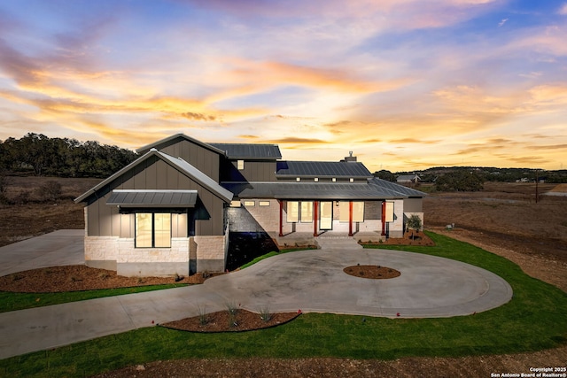 back of property at dusk featuring roof mounted solar panels, covered porch, curved driveway, and metal roof
