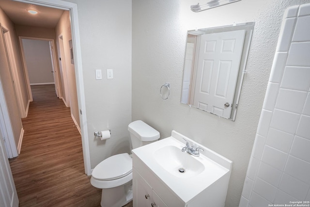 bathroom with baseboards, wood finished floors, toilet, and vanity