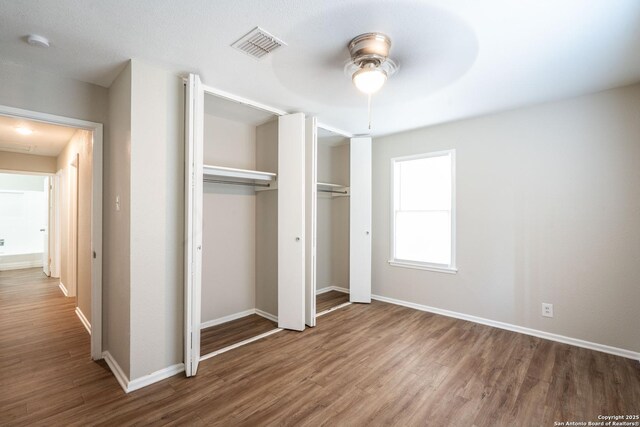 unfurnished bedroom with ceiling fan, baseboards, wood finished floors, and visible vents