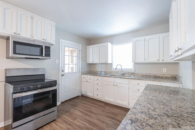 kitchen featuring wood finished floors, appliances with stainless steel finishes, white cabinetry, and a sink