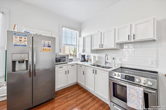 kitchen featuring stainless steel appliances, a sink, dark wood finished floors, tasteful backsplash, and white cabinetry