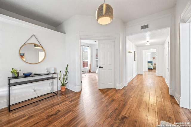hallway with wood finished floors, visible vents, and baseboards