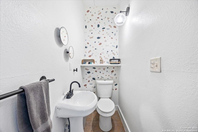 half bathroom featuring baseboards, a sink, tile patterned flooring, and toilet