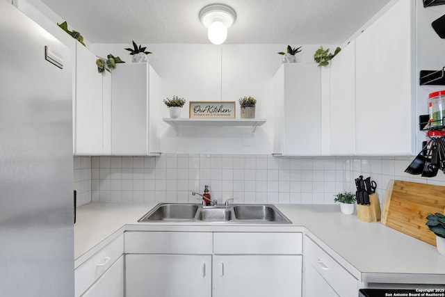 kitchen featuring white cabinets, light countertops, a sink, freestanding refrigerator, and decorative backsplash