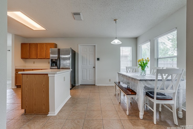 kitchen featuring a textured ceiling, visible vents, brown cabinetry, stainless steel refrigerator with ice dispenser, and light countertops