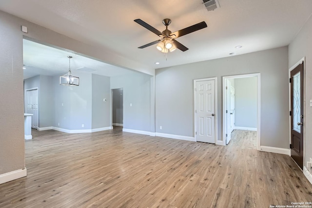 unfurnished living room with baseboards, ceiling fan with notable chandelier, visible vents, and light wood-style flooring