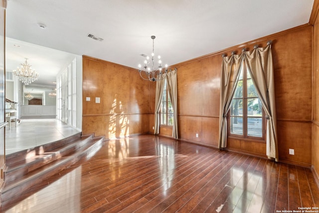 spare room with an inviting chandelier, ornamental molding, wood finished floors, and visible vents