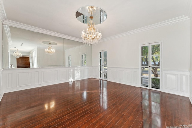 empty room featuring wood finished floors, ornamental molding, a decorative wall, wainscoting, and a chandelier
