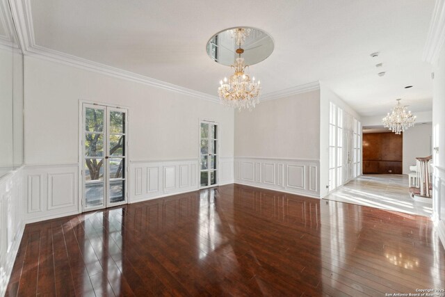 unfurnished dining area with a decorative wall, crown molding, hardwood / wood-style flooring, wainscoting, and a chandelier
