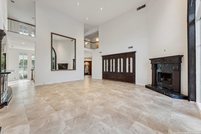 unfurnished living room featuring visible vents, baseboards, a towering ceiling, and a high end fireplace
