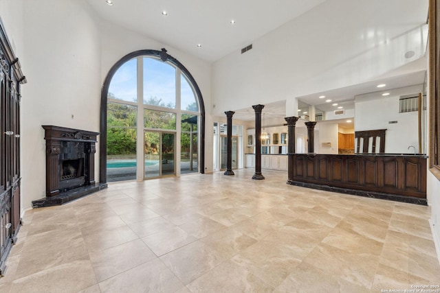 unfurnished living room with a high end fireplace, decorative columns, a towering ceiling, visible vents, and recessed lighting