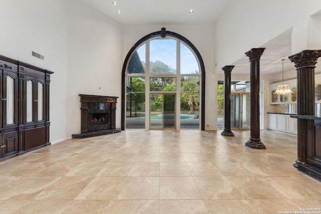 unfurnished living room with a high ceiling, a high end fireplace, visible vents, decorative columns, and a notable chandelier