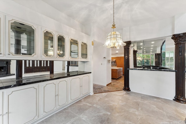kitchen featuring dark countertops, a chandelier, glass insert cabinets, pendant lighting, and white cabinetry