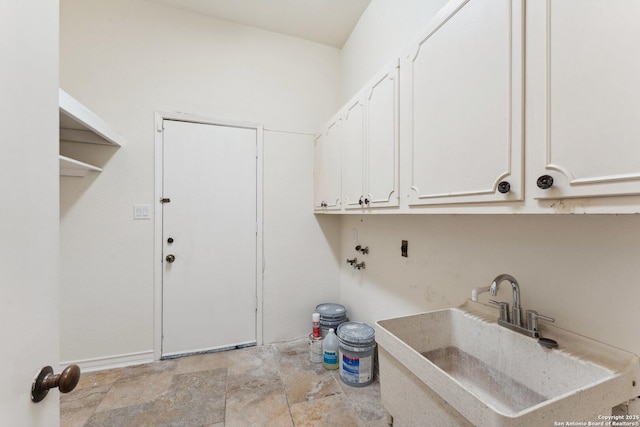 laundry room featuring stone finish floor, a sink, hookup for a washing machine, baseboards, and cabinet space