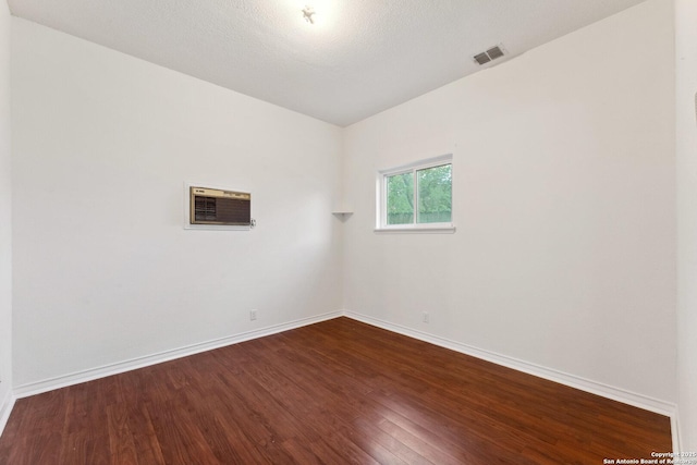 empty room with a wall mounted air conditioner, visible vents, baseboards, and dark wood-style flooring