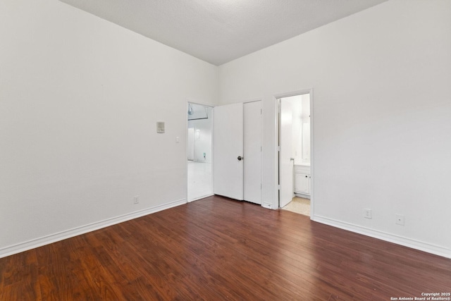 unfurnished bedroom with ensuite bath, baseboards, and wood finished floors