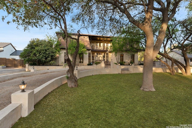 view of front of home with a front yard, a balcony, and fence