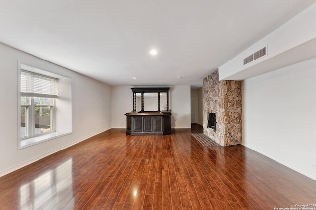 unfurnished living room with baseboards, wood finished floors, a stone fireplace, and visible vents