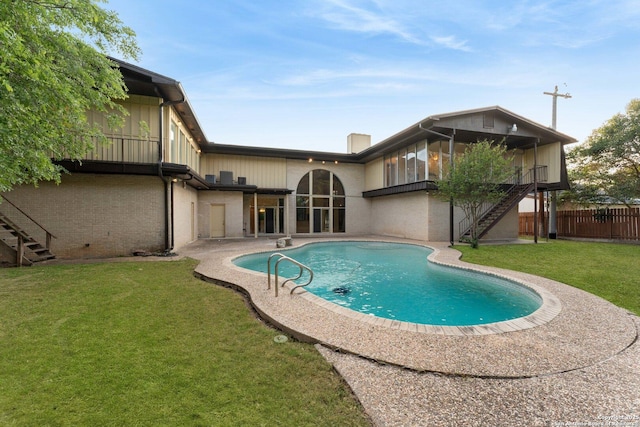 back of property with stairway, a fenced in pool, fence, a lawn, and brick siding