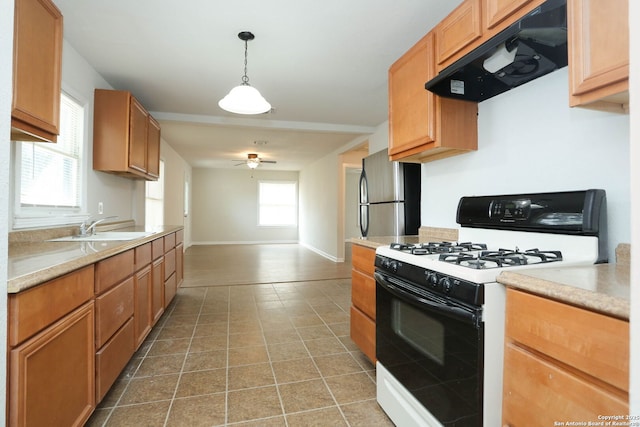 kitchen featuring range with gas cooktop, a sink, light countertops, under cabinet range hood, and freestanding refrigerator