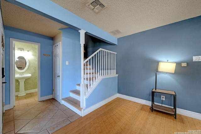 stairway featuring a textured ceiling, baseboards, visible vents, and ornate columns