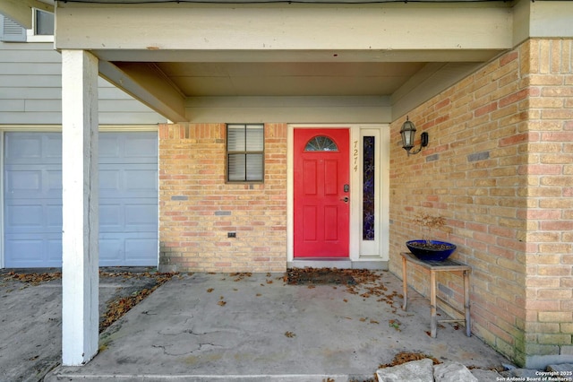 doorway to property with an attached garage and brick siding