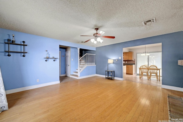 unfurnished living room with stairway, visible vents, baseboards, light wood-style flooring, and ceiling fan with notable chandelier