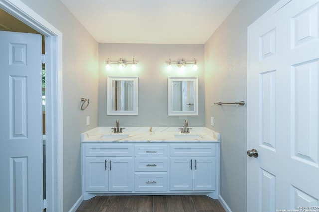 full bath with baseboards, wood finished floors, a sink, and double vanity