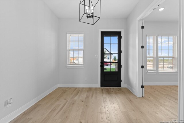 doorway with light wood-style flooring, baseboards, a wealth of natural light, and a chandelier