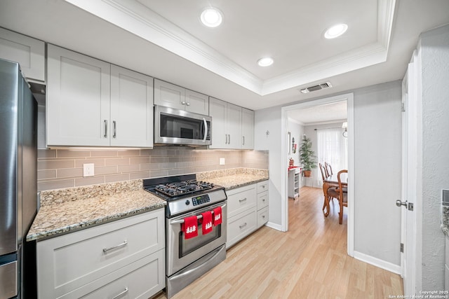 kitchen with stainless steel appliances, a tray ceiling, light wood-type flooring, visible vents, and backsplash
