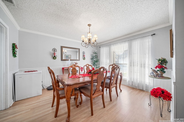 dining space with visible vents, light wood-type flooring, wainscoting, a textured ceiling, and a notable chandelier