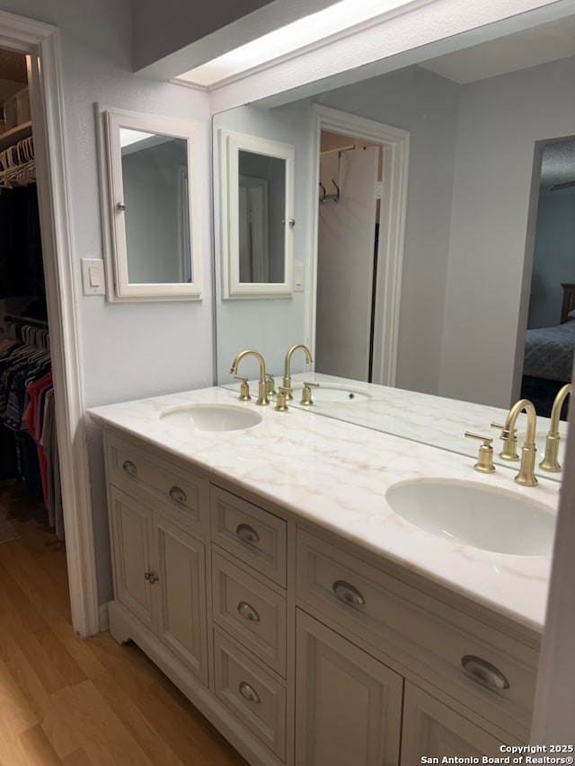 ensuite bathroom featuring double vanity, wood finished floors, and a sink