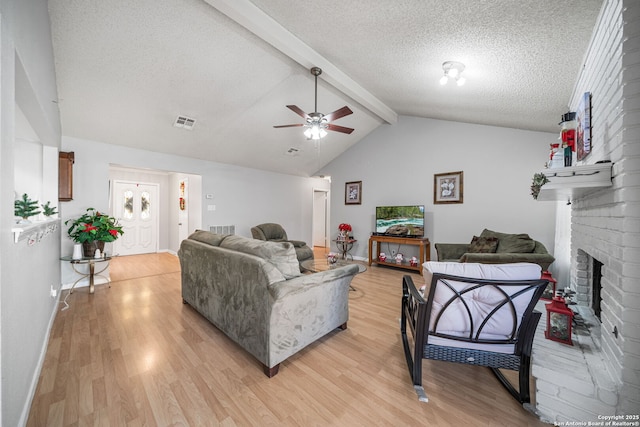 living area featuring ceiling fan, a brick fireplace, a textured ceiling, and light wood finished floors