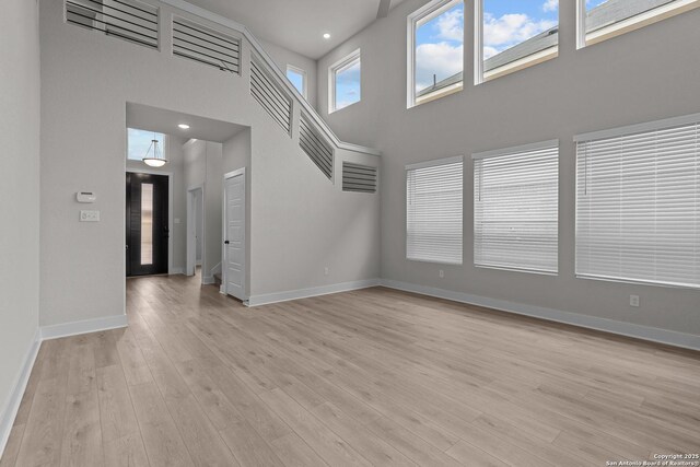 133 Bailey Blf, San Antonio, TX 78253 - unfurnished living room featuring light wood-style floors, a towering ceiling, and baseboards