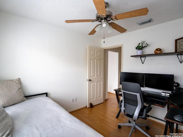 bedroom featuring light wood-type flooring, visible vents, a textured ceiling, and ceiling fan
