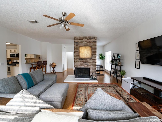 living room featuring wood finished floors, visible vents, a textured ceiling, and ceiling fan