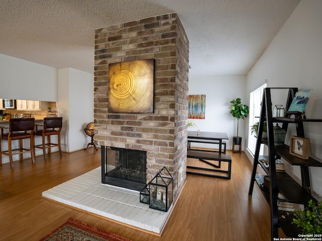 living area with a brick fireplace, wood finished floors, and a textured ceiling