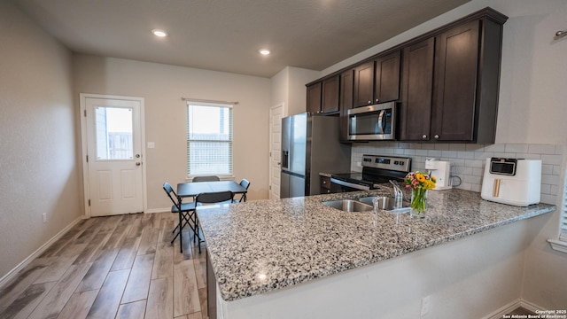 kitchen featuring light wood-type flooring, dark brown cabinetry, backsplash, light stone countertops, and appliances with stainless steel finishes
