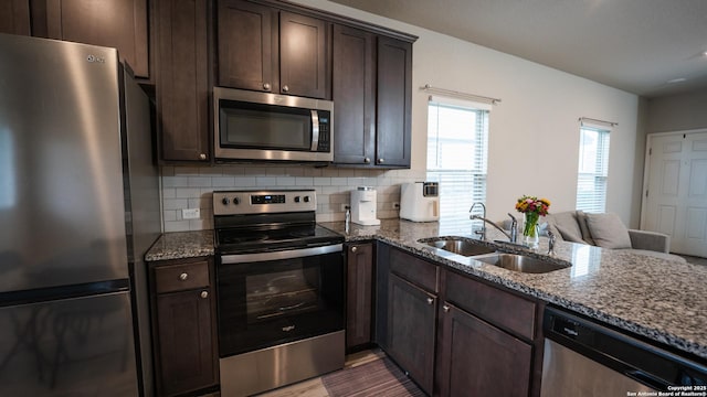kitchen with backsplash, a sink, stone counters, dark brown cabinetry, and appliances with stainless steel finishes