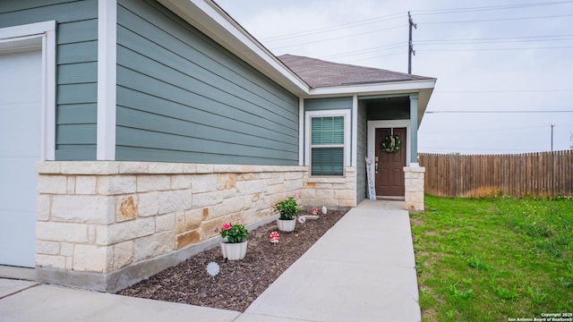 doorway to property with a lawn, fence, stone siding, and a shingled roof